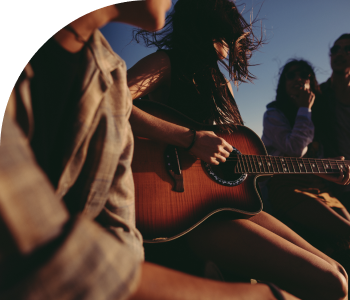 A woman strumming the guitar with other people listening to her performance.